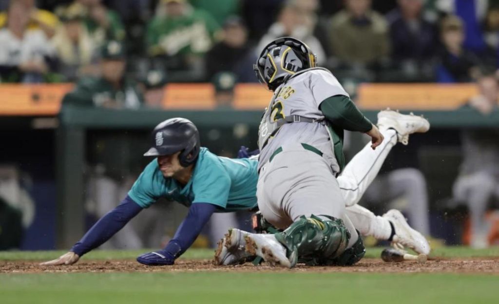 El lanzador de los Marineros de Seattle Leo Rivas anota mientras el receptor de los Atléticos de Oakland Shea Langeliers se estira para tocar la pelota durante la décima entrada en un partido de béisbol, el sábado 28 de septiembre de 2024, en Seattle. Los Marineros ganaron 7-6. (Foto AP/John Froschauer)